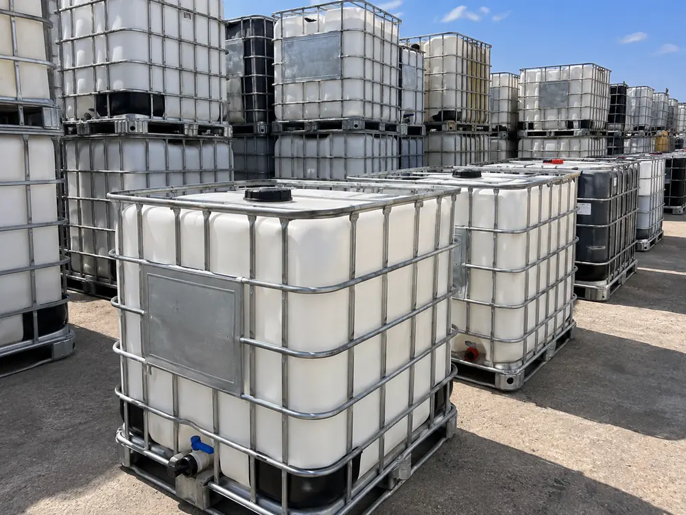 Clean reconditioned white IBC totes stacked two high in an outdoor yard under blue sky