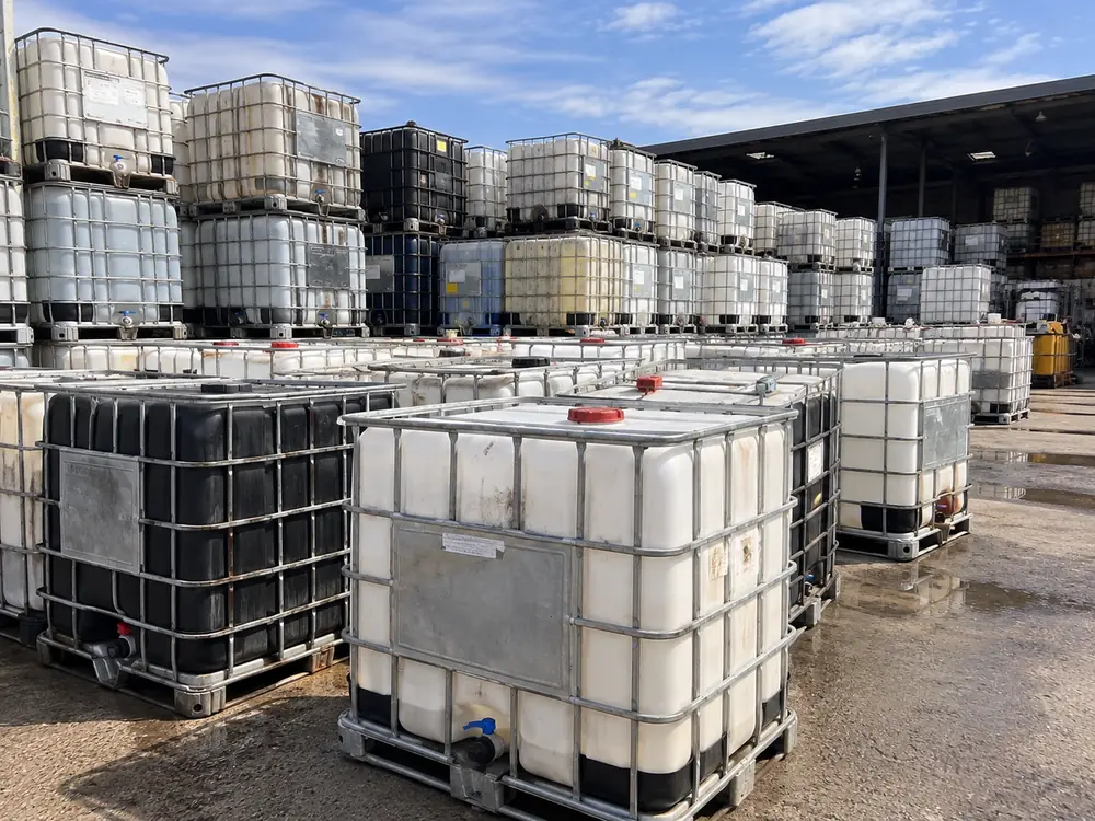 Mixed used IBC totes awaiting inspection, some stained and discoloured, beside a covered shed