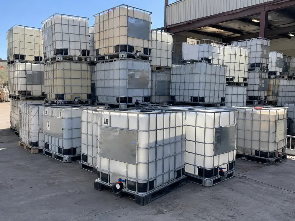 Used IBC totes stacked beside the yard building, awaiting washing